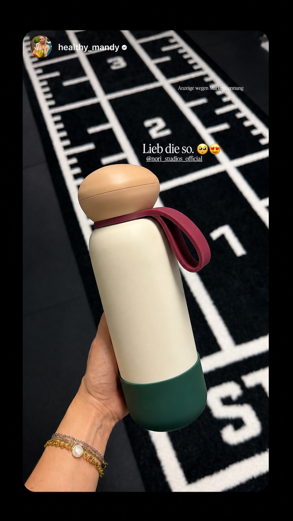 Cream and green nori bottle with a maroon loop, held above a gym floor