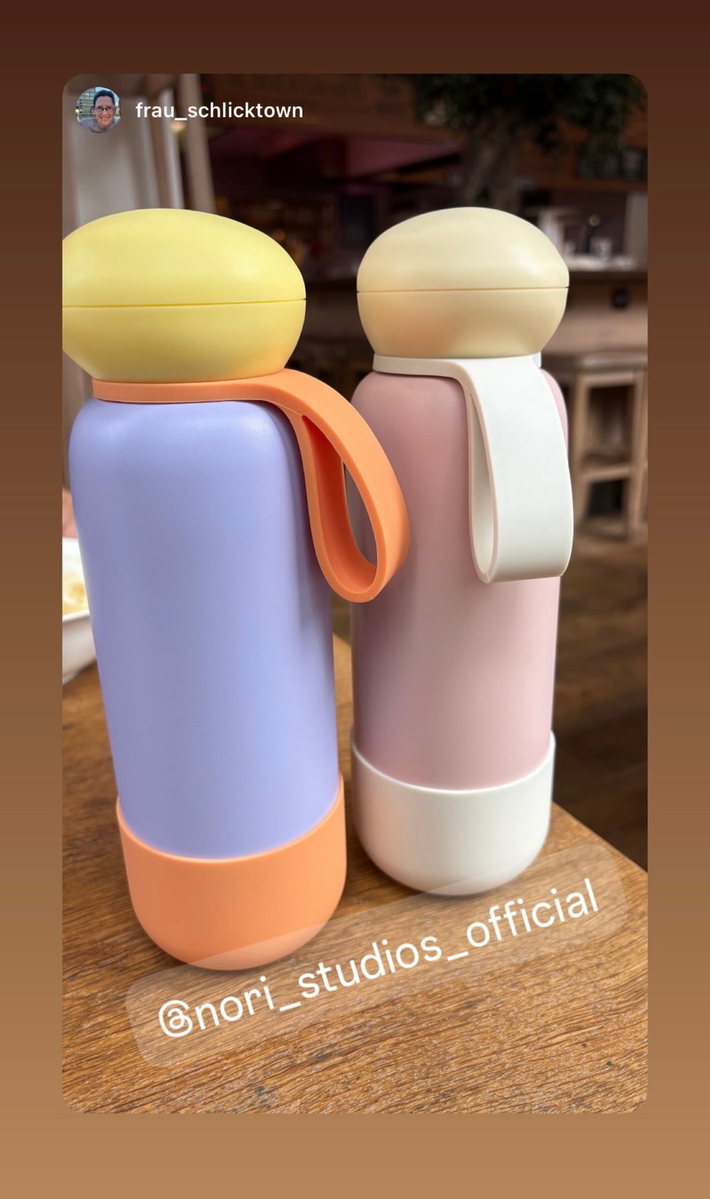 Two nori bottles, one lilac with orange and one pink with white, on a wooden table
