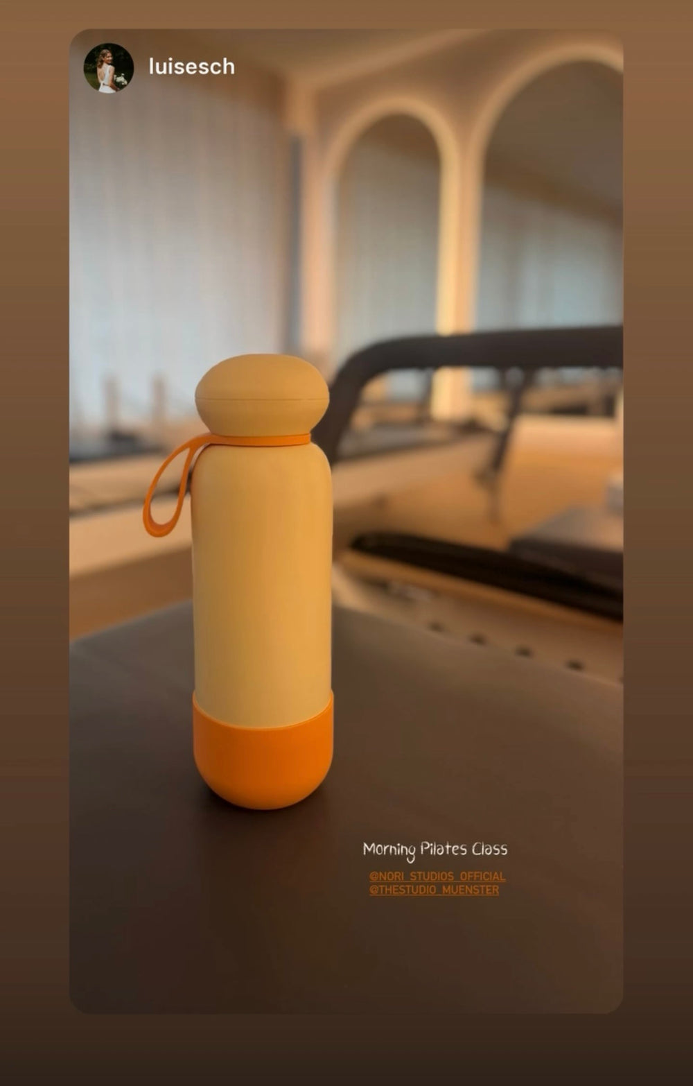 Yellow and orange nori bottle resting on a reformer in a pilates studio