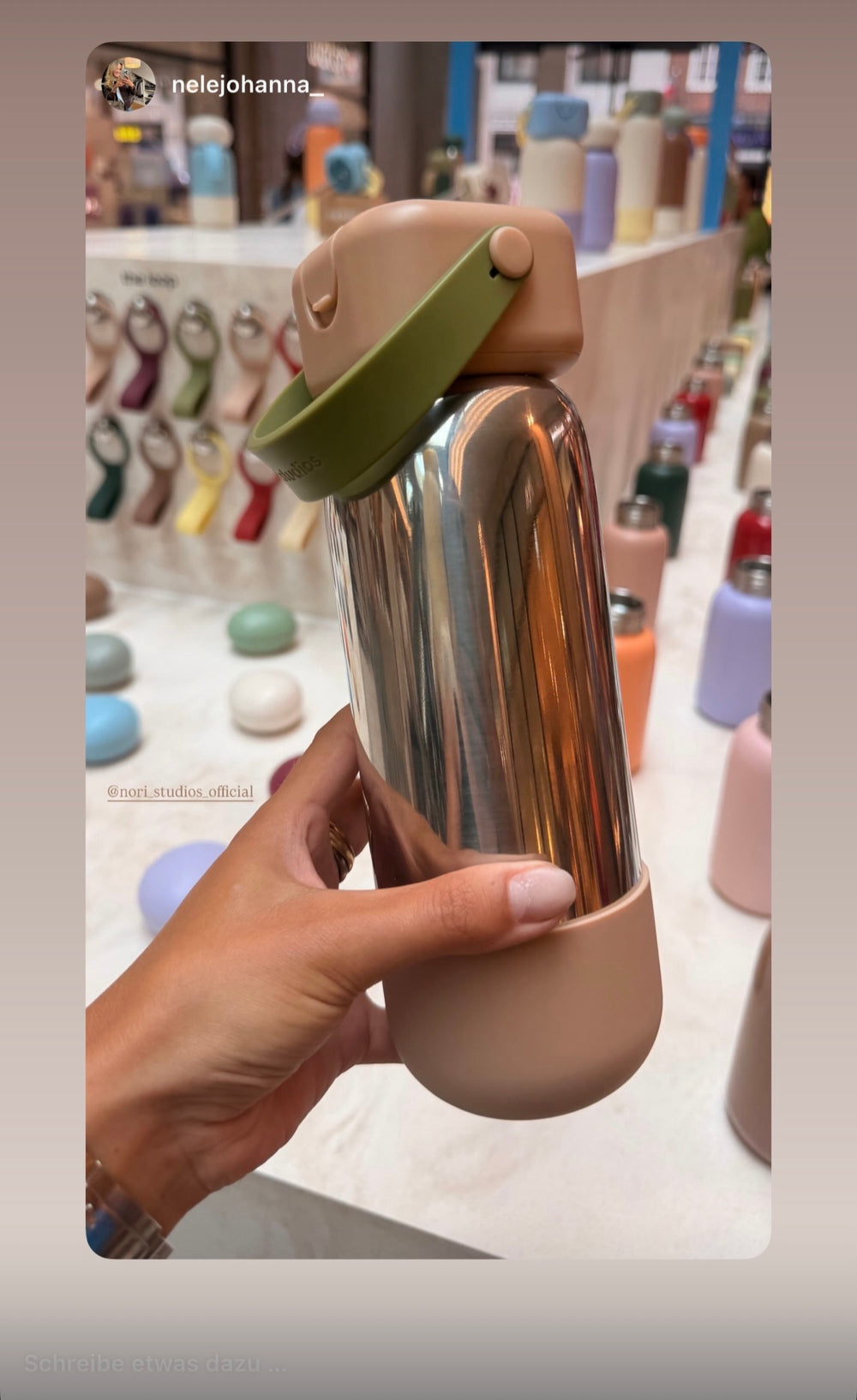 Chrome nori bottle with a sage cap, held in front of the in-store colour wall