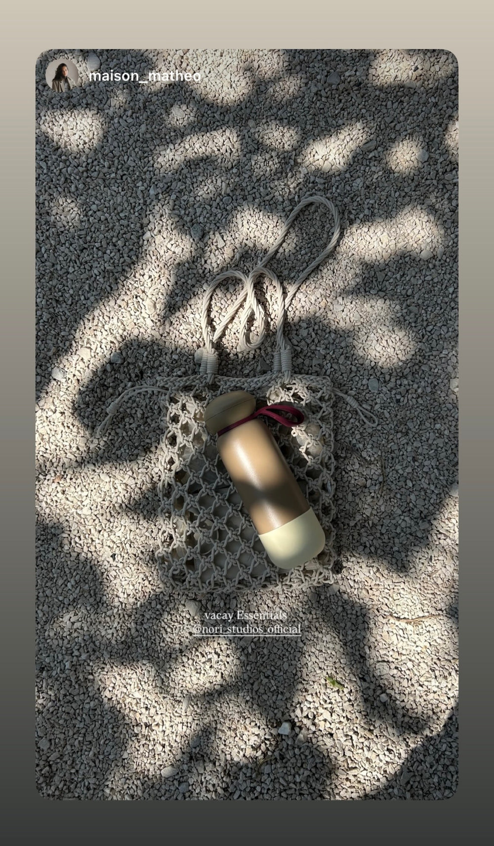 Cream nori bottle in a mesh bag, laid on sand in dappled light