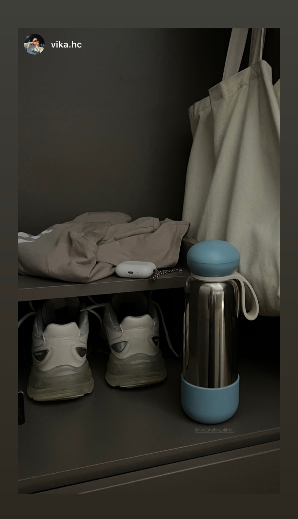 Chrome nori bottle with a blue boot on a hallway shelf beside trainers and a tote