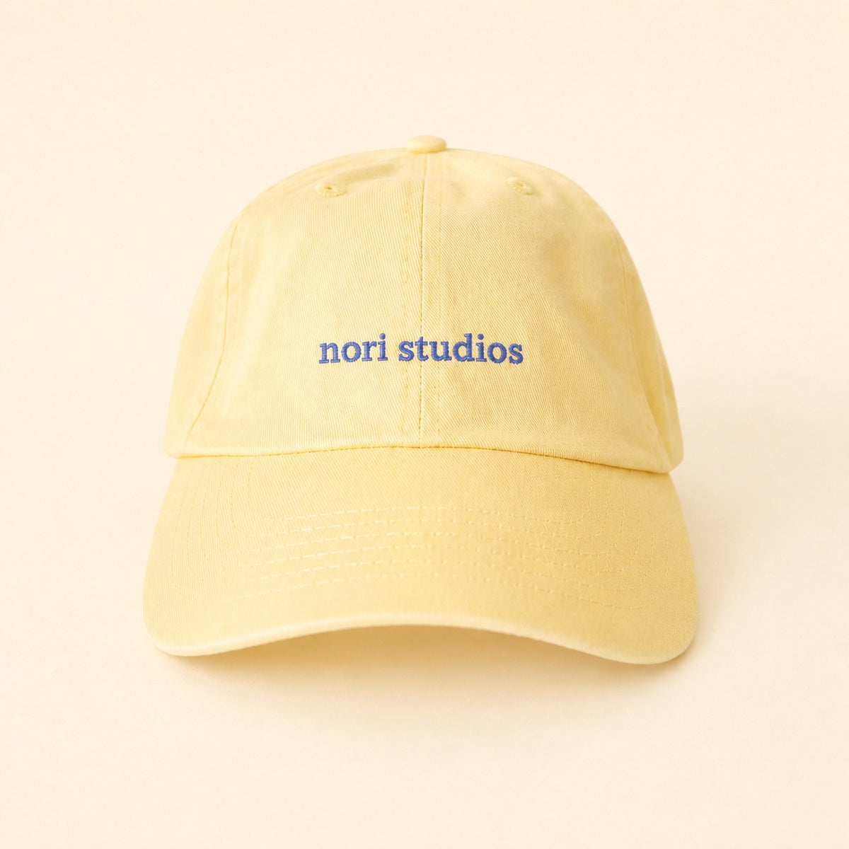 Butter yellow nori studios cap with a blue embroidered wordmark